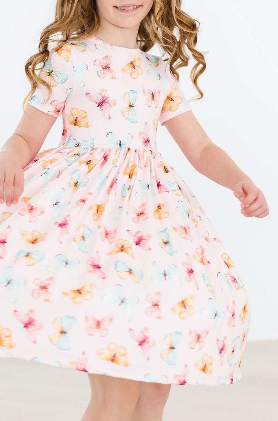young girl wearing a pink butterfly print twirl dress for girls spinning around with a smile