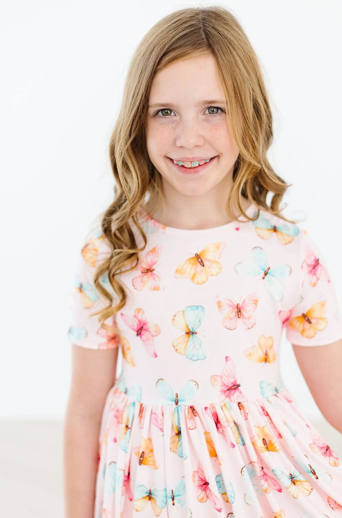 Smiling girl wearing a pink butterfly print twirl dress for girls with short sleeves posing indoors