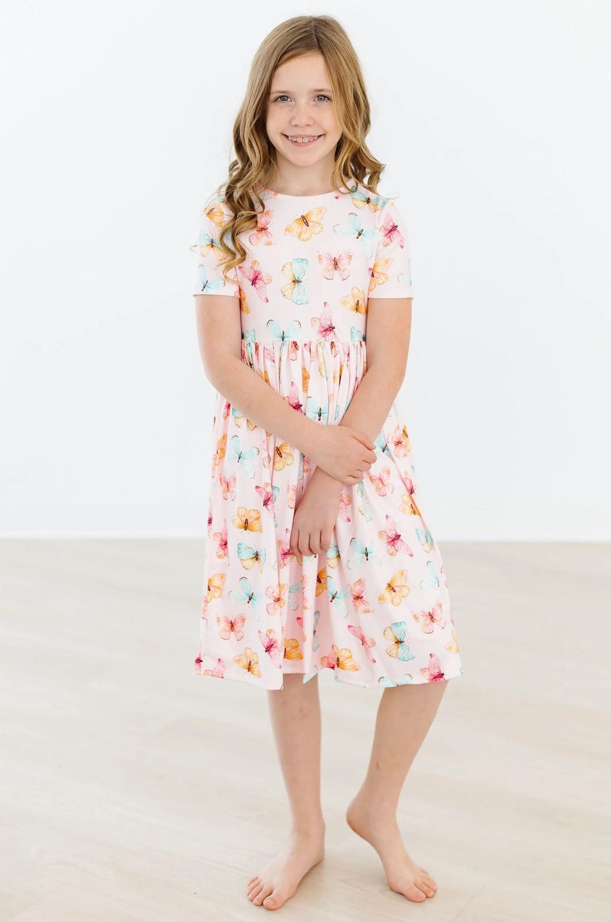 Young girl wearing a white butterfly print twirl dress for girls standing and smiling indoors