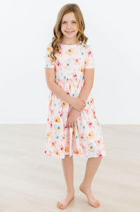 Young girl wearing a white butterfly print twirl dress for girls standing and smiling indoors
