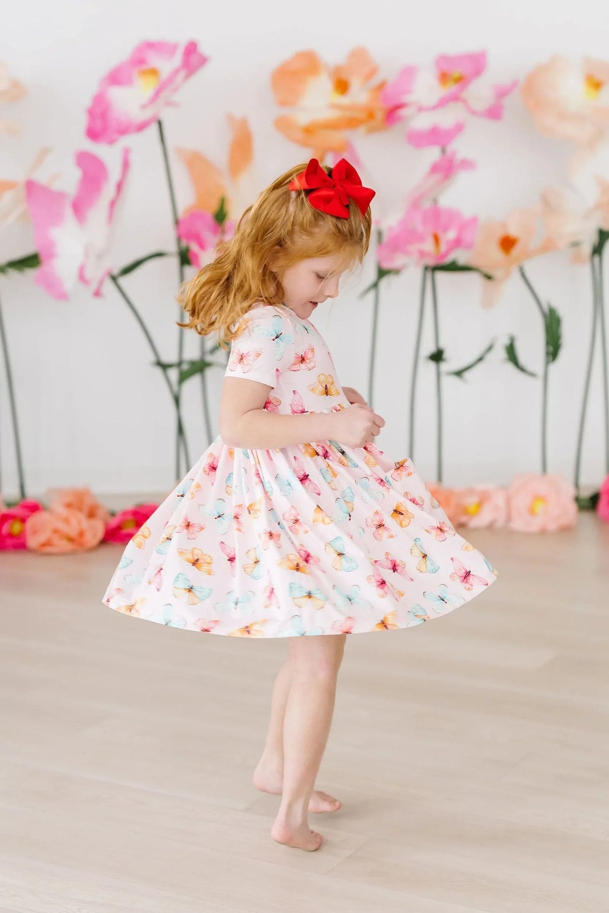 Young girl wearing white butterfly print twirl dress for girls spinning indoors with floral backdrop