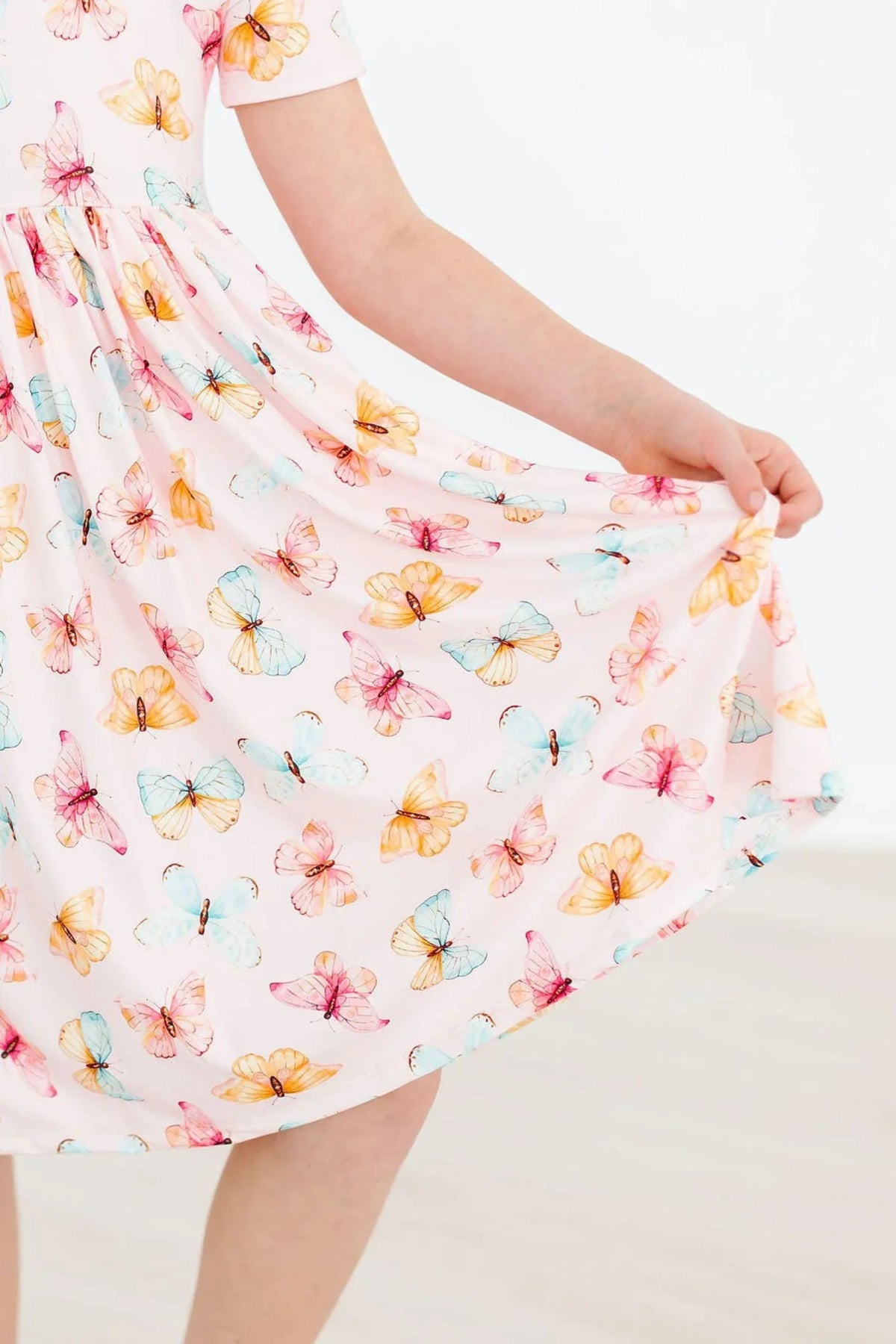 Young girl wearing white butterfly print twirl dress for girls holding the skirt out