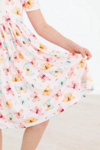 Young girl wearing white butterfly print twirl dress for girls holding the skirt out