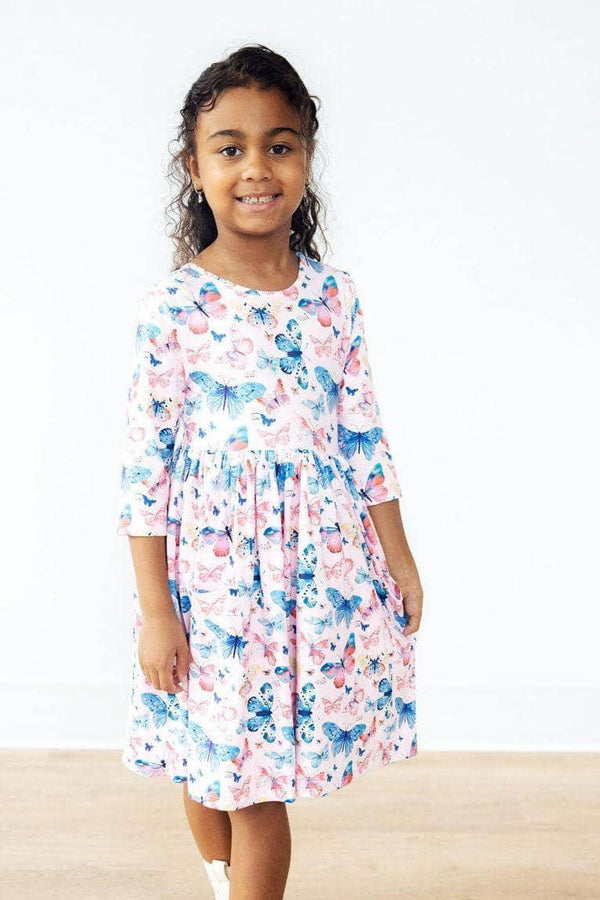 Girl wearing pink and blue butterfly twirl dress for girls with sleeves smiling and posing