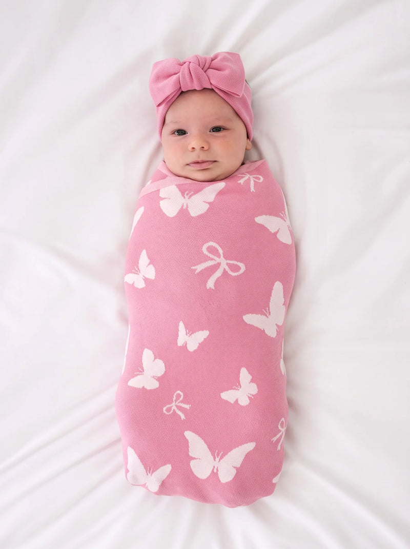Newborn wrapped in pink butterfly blanket wearing matching headband on white sheet