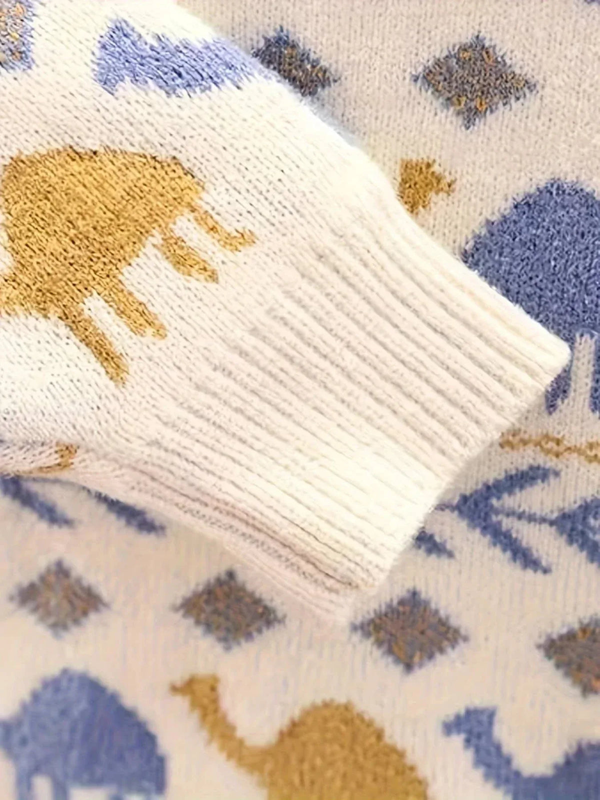 Close-up of white boys knit sweater with blue and yellow dinosaur patterns on sleeve and body