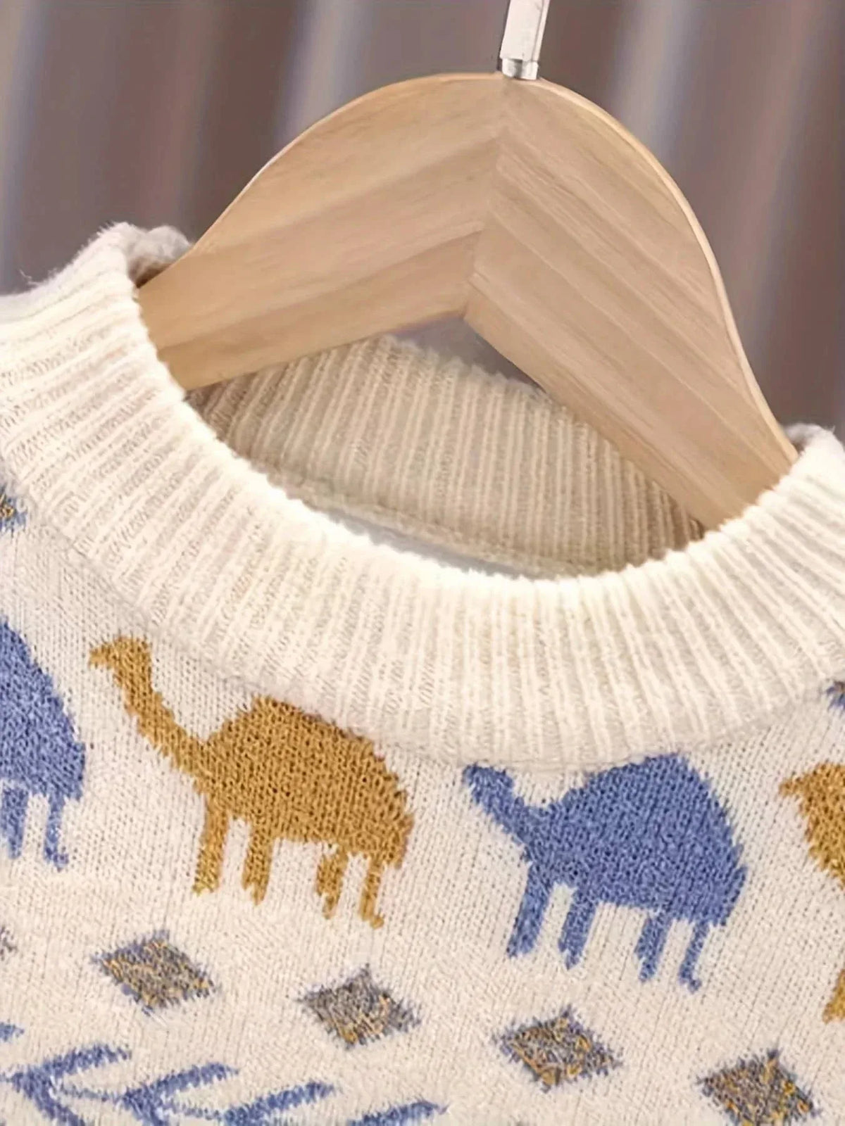 Close-up of white boys knit sweater with blue and yellow dinosaur pattern hanging on wooden hanger
