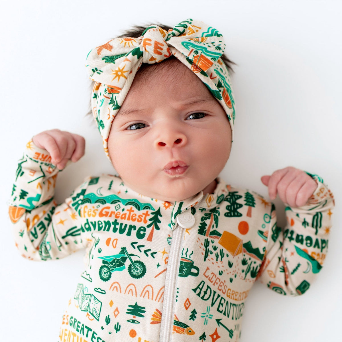 Baby wearing a onesie with 'Let's Greatest Adventure' text and graphics, and a matching headband.