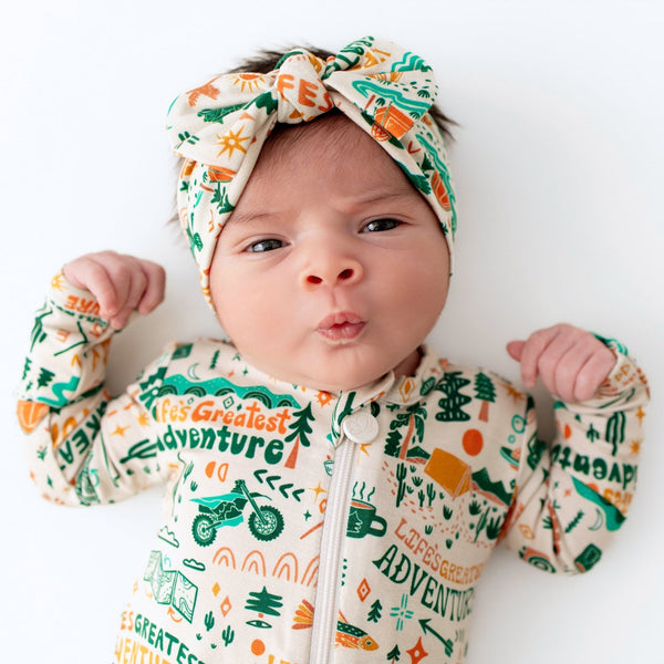 Baby wearing a onesie with 'Let's Greatest Adventure' text and graphics, and a matching headband.