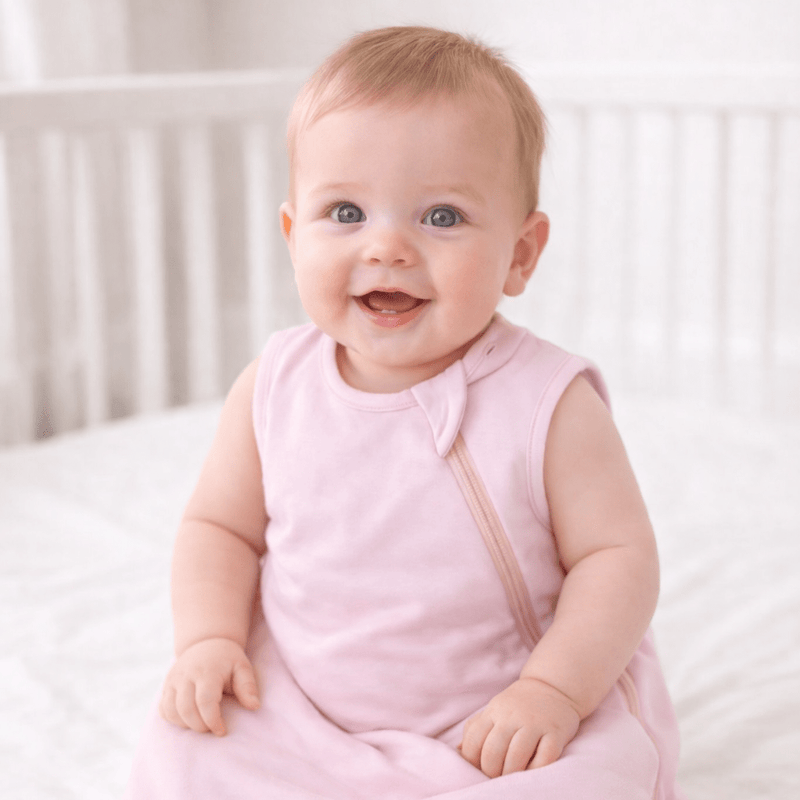 Baby in a pink outfit sitting on a white bed
