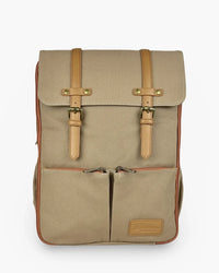 Beige rugged canvas diaper backpack with tan leather straps, brass buckles, and rust zipper trim on front pocket