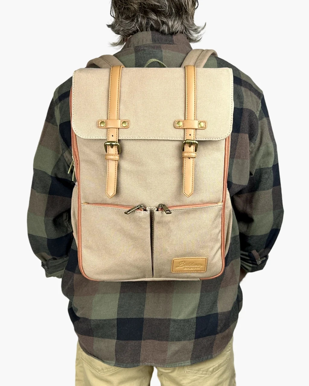 Rear lifestyle view of person carrying beige diaper backpack featuring vintage design, leather straps, brass buckles, and