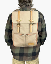 Rear lifestyle view of person carrying beige diaper backpack featuring vintage design, leather straps, brass buckles, and