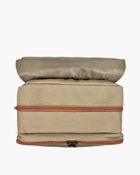 Top-down view of open beige canvas diaper backpack revealing dual compartments, terracotta zippers, and padded flap
