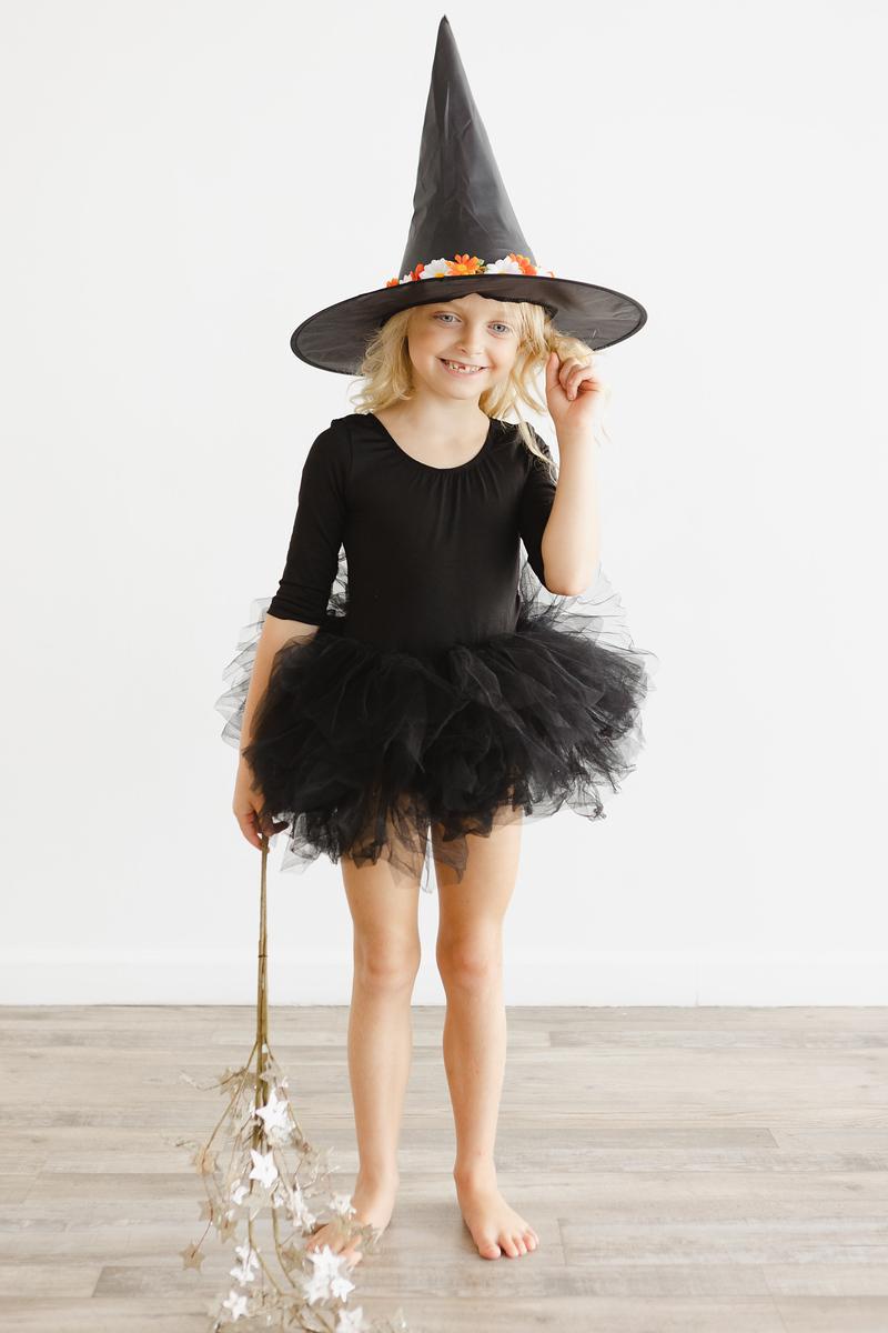 A young dancer in a Black 3/4 Tutu Leotard by Mila & Rose, striking a fun pose with a witch hat, radiating confidence and joy.