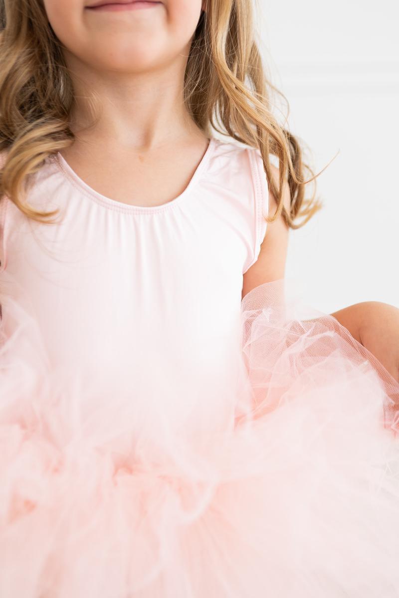 Close-up of a girl's upper body, highlighting the soft fabric of the 'Elana' Ballet Pink Tank Tutu Leotard with a fluffy tutu skirt.