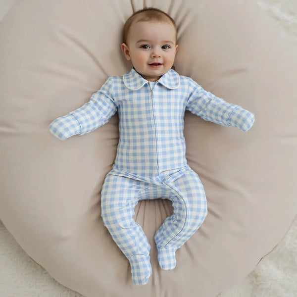 Baby wearing blue and white checked baby zippered footie romper lying on beige cushion smiling