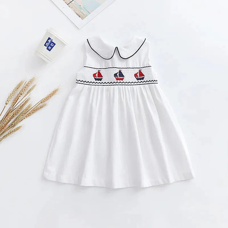 white baby party dress with black trim and embroidered red and blue sailboats sleeveless