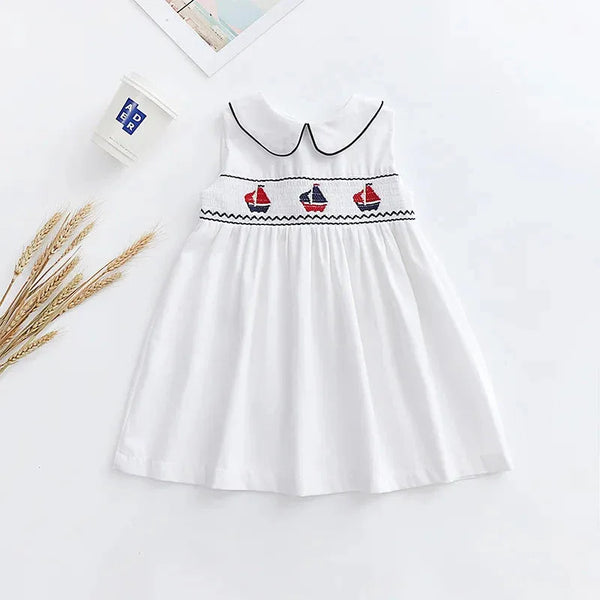 white baby party dress with black trim and embroidered red and blue sailboats sleeveless