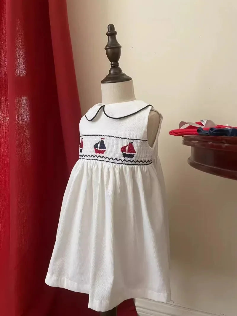White sleeveless baby party dress with navy and red sailboat embroidery and peter pan collar