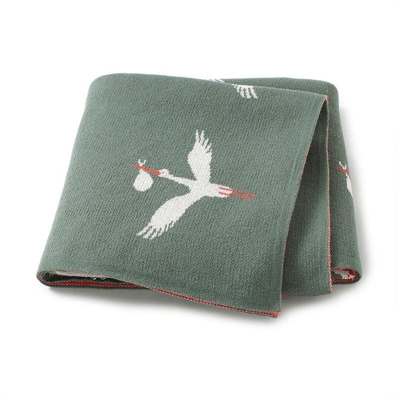 green children's knit blanket with white stork carrying a bundle design for babies and kids