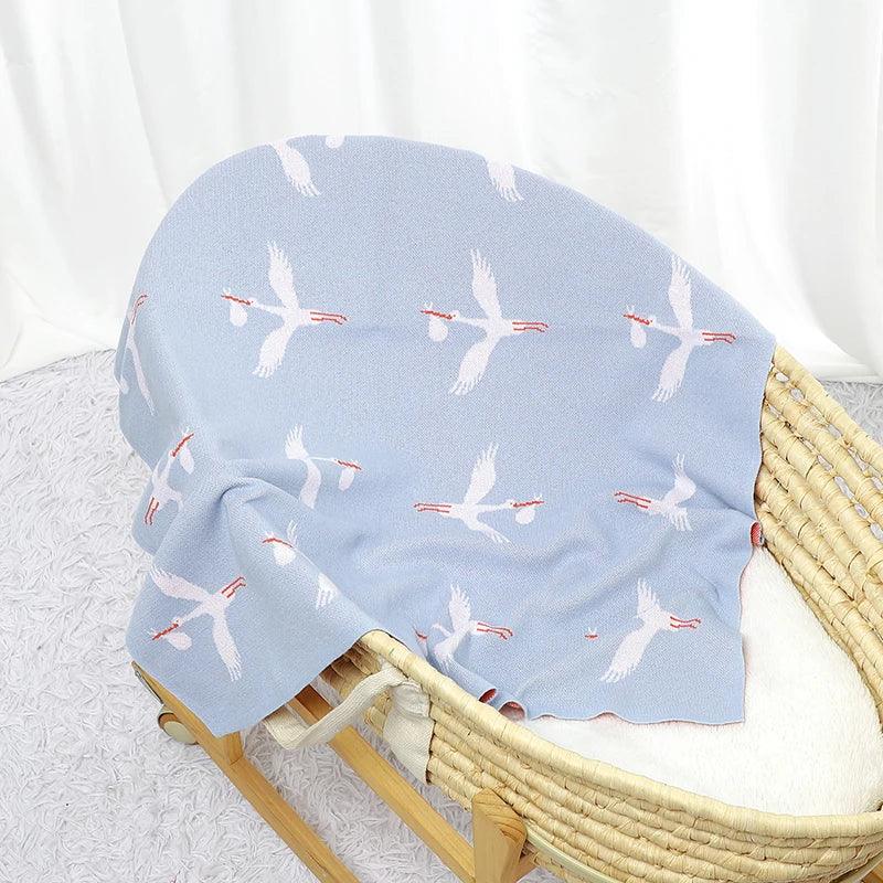 Light blue children's knit blanket with white stork bird pattern draped over a woven bassinet
