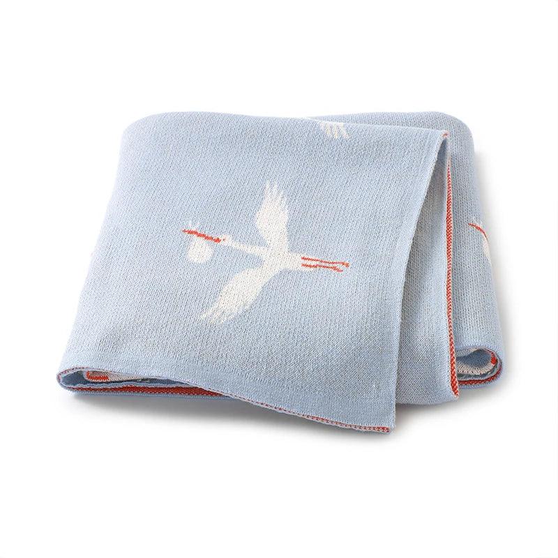 Light blue children's knit blanket with white stork design and red trim for babies and kids