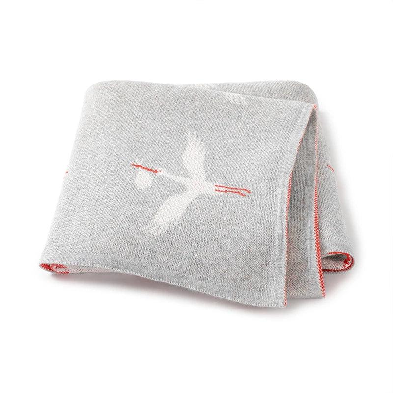 Gray children's knit blanket with white stork design and red edge stitching for babies and kids