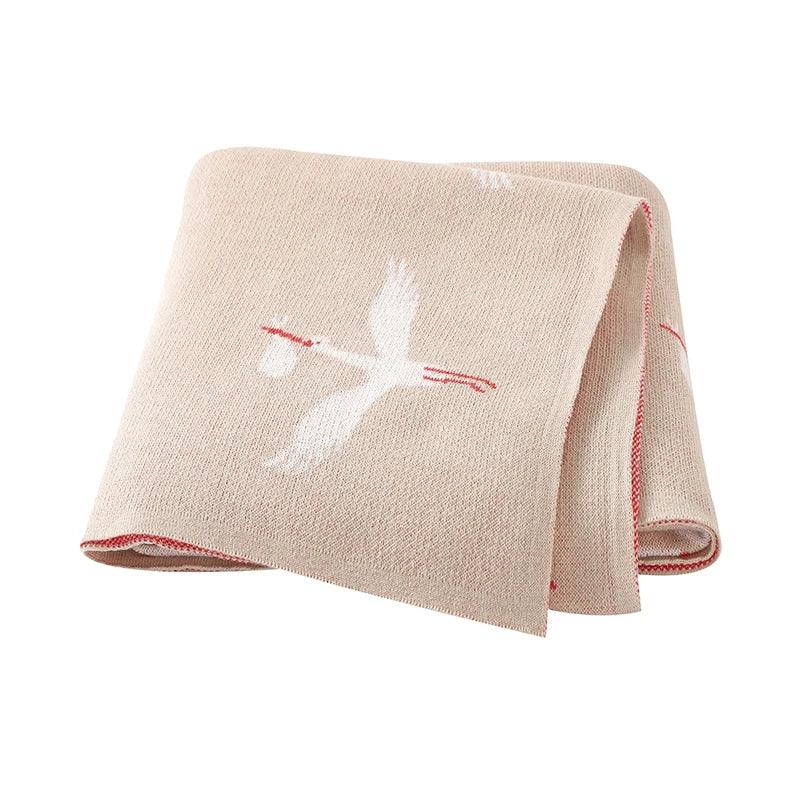 Beige children's knit blanket with white stork design and red trim for babies and toddlers
