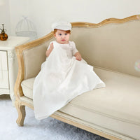 baby boy in white christening gown for boys with cap sitting on beige vintage sofa