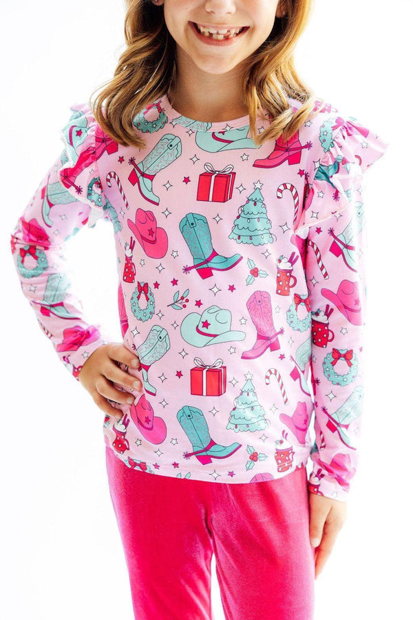 girl wearing pink Christmas cowgirl ruffle tee long sleeve top with holiday boots and gifts print