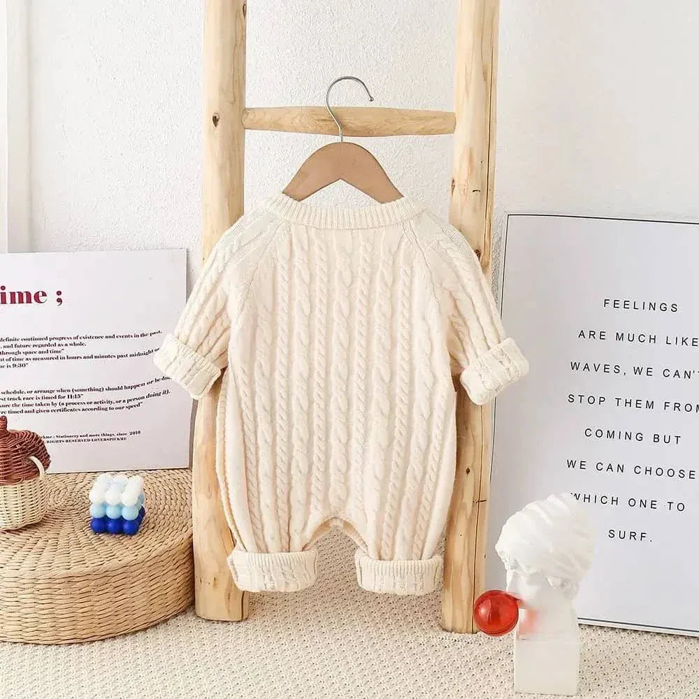 cream classic cable knit baby romper for infants displayed hanging on wooden rack