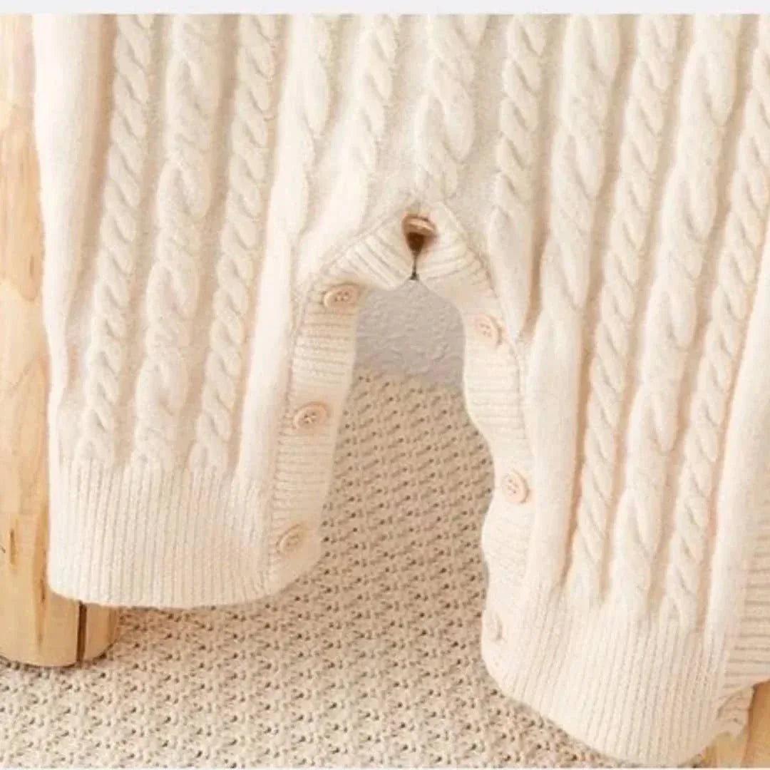 cream classic cable knit baby romper for infants with button closure sitting on textured surface