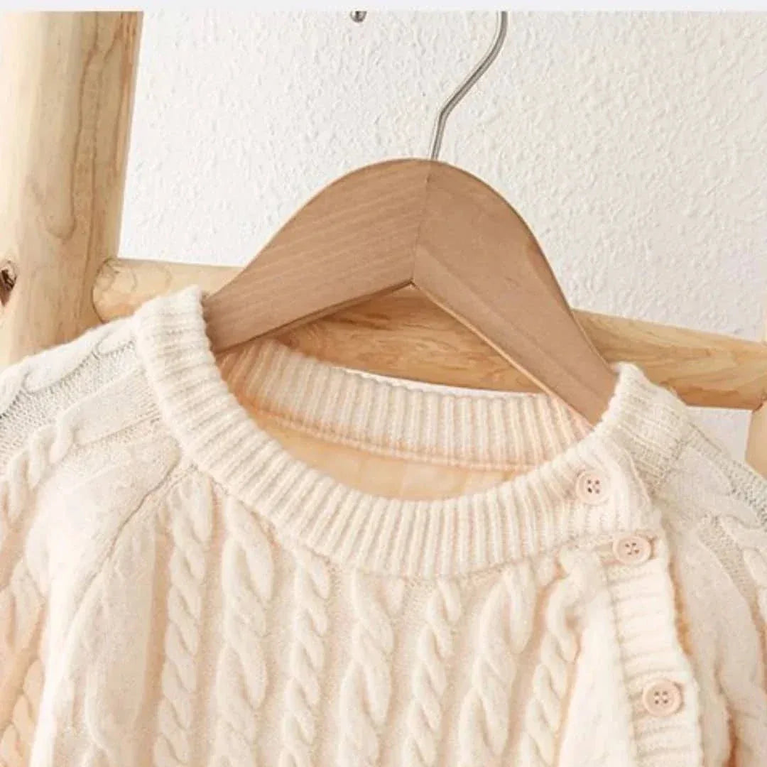 Cream classic cable knit baby romper for newborns hanging on wooden hanger