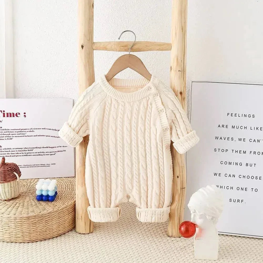 cream classic cable knit baby romper hanging on wooden hanger for infants