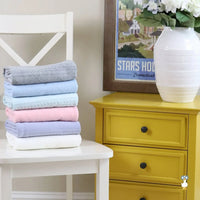 Lavender knit baby blanket made of soft material folded on white chair with other pastel blankets