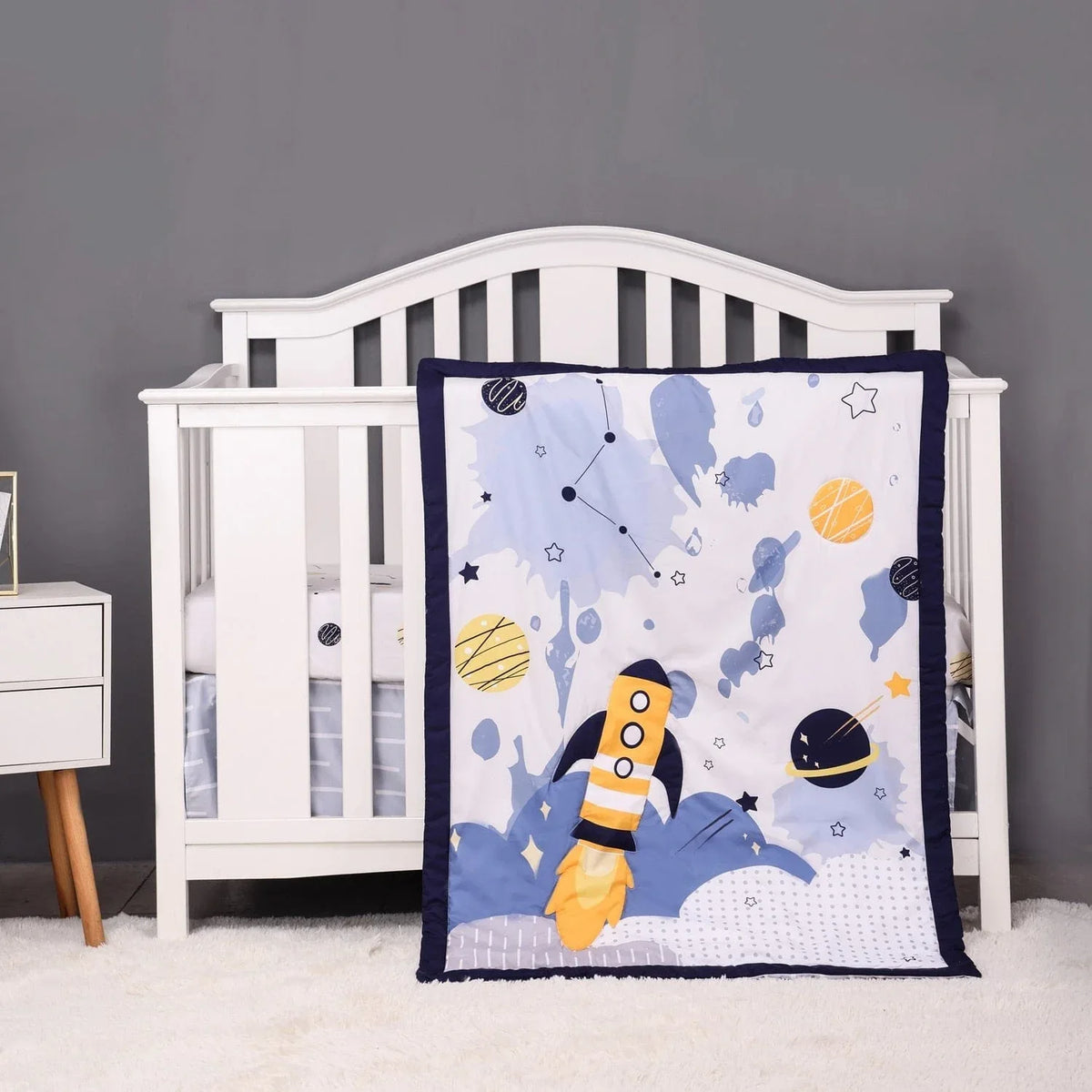 baby comfort set with blue and yellow space rocket design hanging on white crib for infants