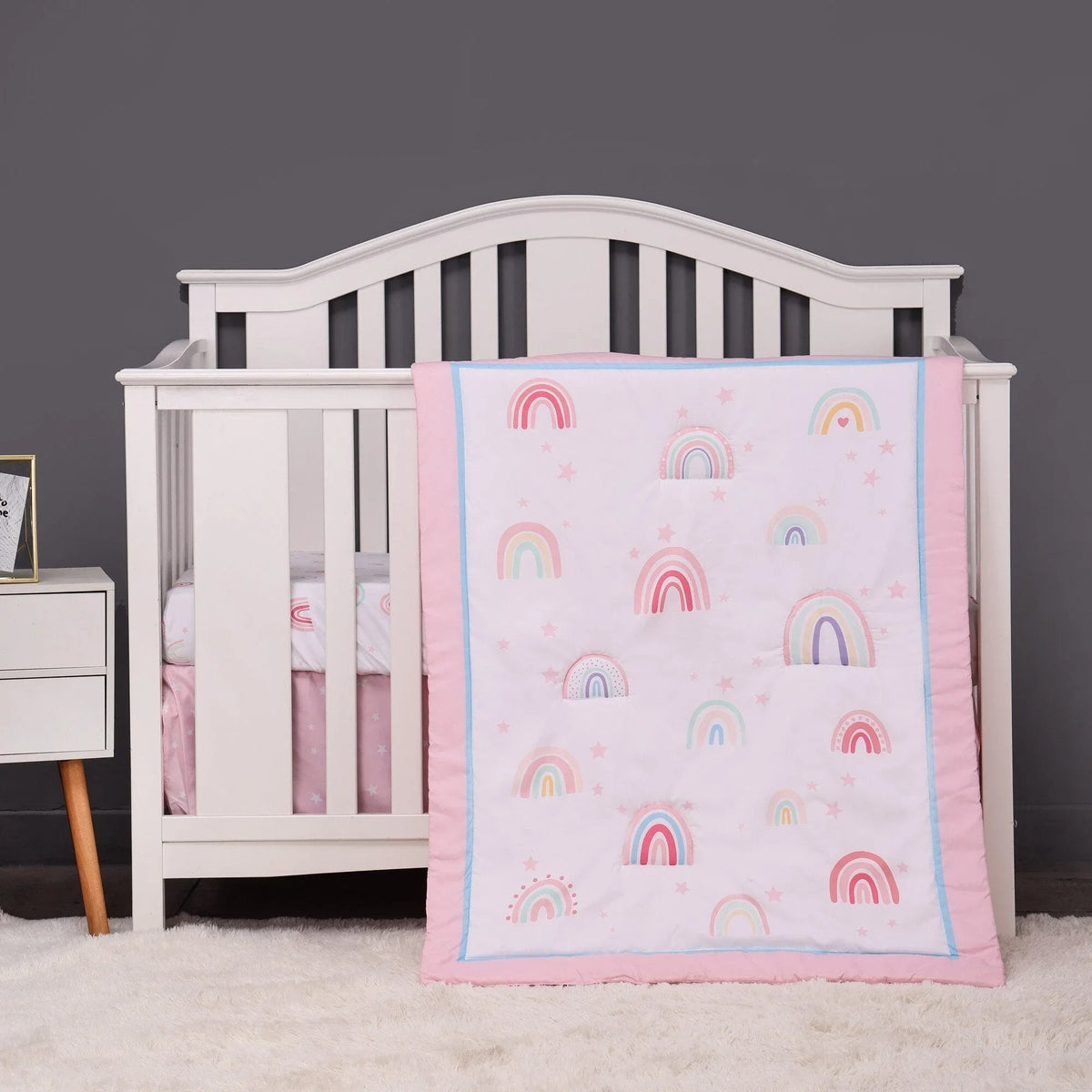 Baby pink comfort set with pastel rainbow patterns for newborns, soft and cozy blanket draped over white crib