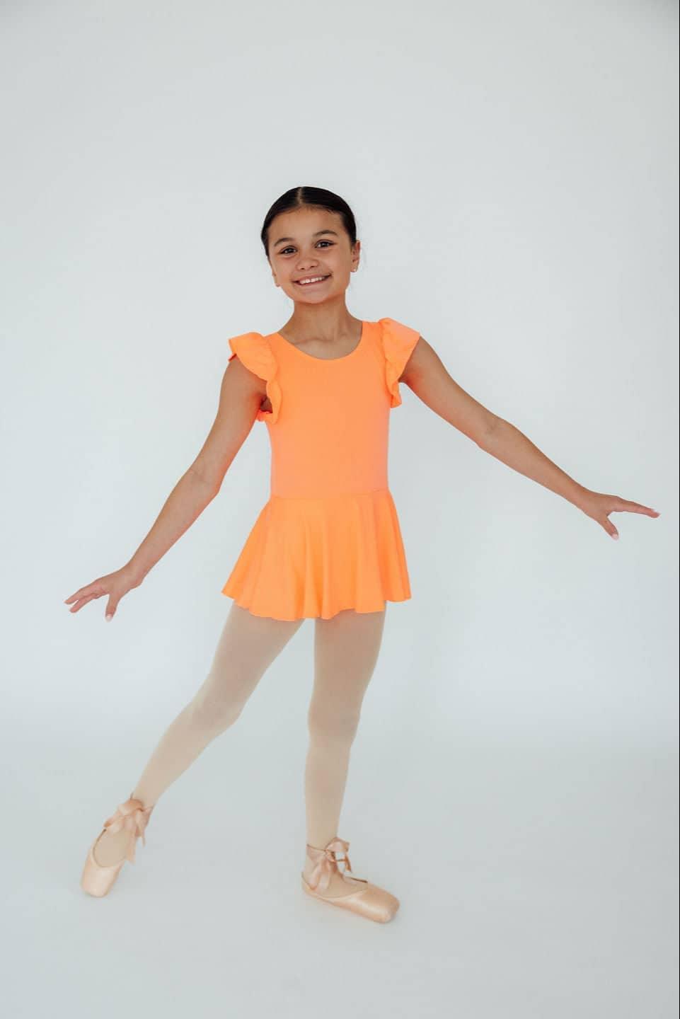 Young girl wearing coral girls short sleeve twirl leotard smiling and posing in ballet shoes