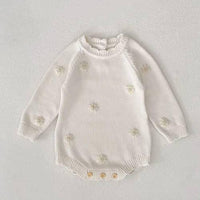 cream cozy knitted baby romper with flower details for infants laid flat on white background
