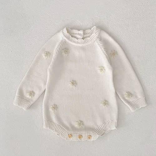 cream cozy knitted baby romper with flower details for infants laid flat on white background