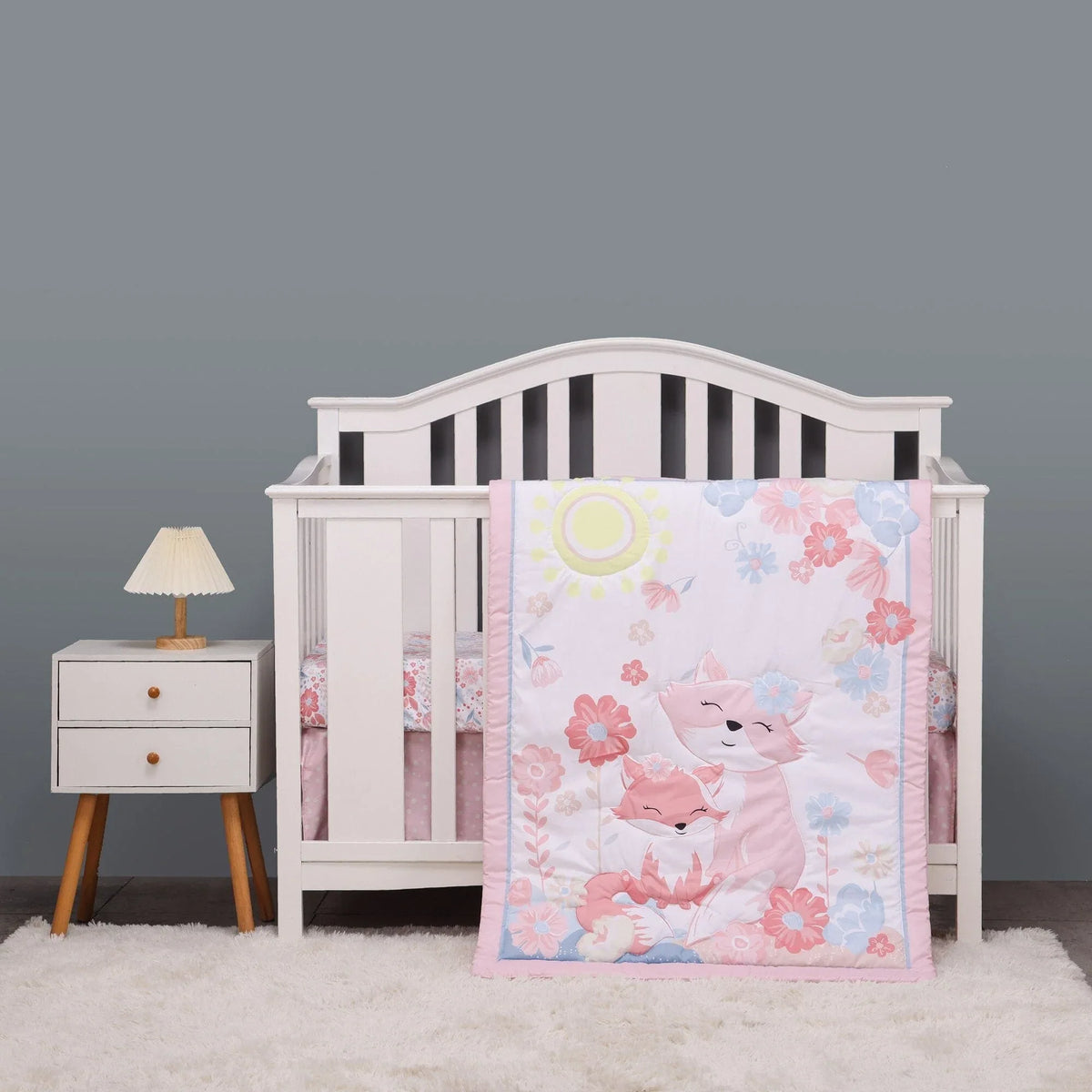 Pink floral crib bedding with fox design for babies in white wooden crib with gray background
