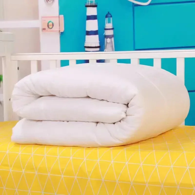 White crib bedding set folded on yellow mattress with geometric pattern for baby nursery