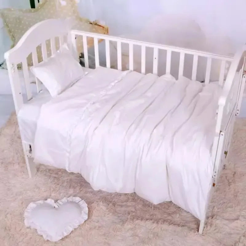 White crib bedding set for baby nursery with soft pillow and ruffled heart-shaped cushion