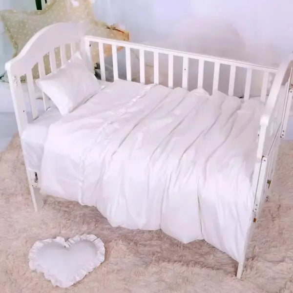 White crib bedding set for baby nursery with soft pillow and ruffled heart-shaped cushion