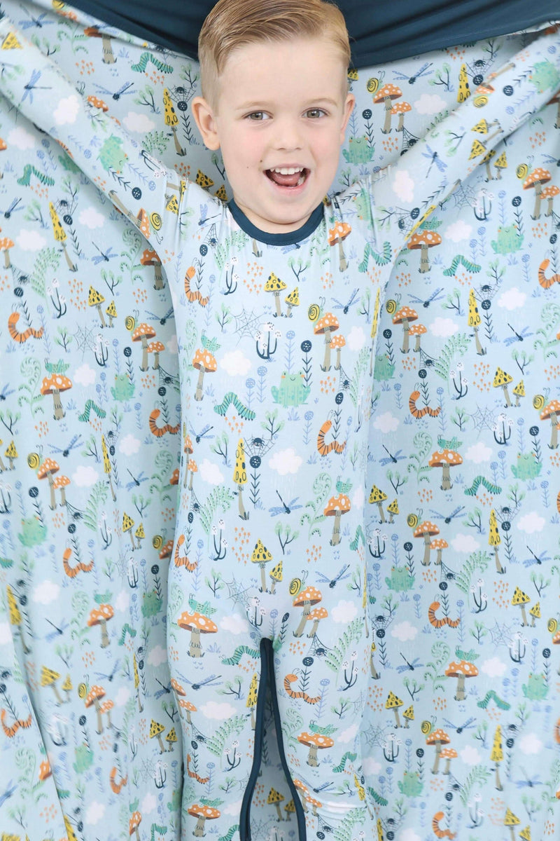 Child wearing a patterned onesie with a forest design, standing inside a fabric display with similar pattern.