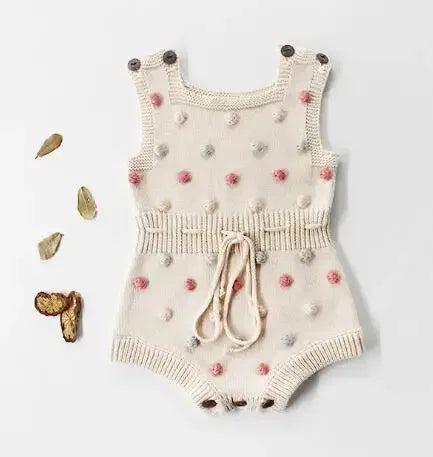 Cute knit baby romper in cream with colorful pom pom details and button straps for infants