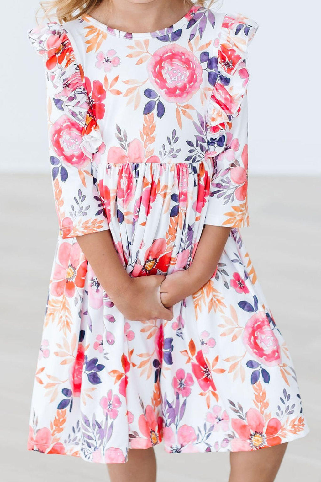 Little girl wearing the Tangerine Leaves 3/4 Sleeve Ruffle Twirl Dress, showcasing vibrant floral patterns and ruffles, perfect for twirling during playtime.