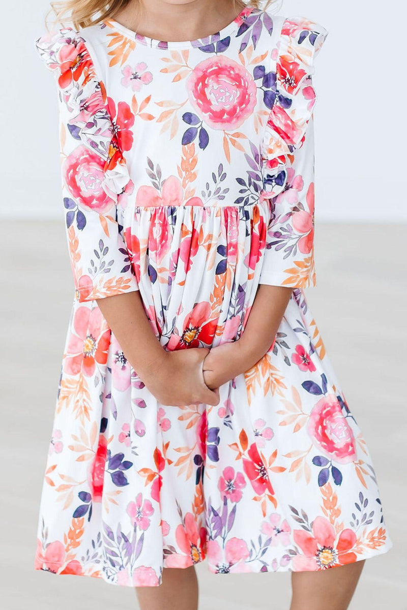 Little girl wearing the Tangerine Leaves 3/4 Sleeve Ruffle Twirl Dress, showcasing vibrant floral patterns and ruffles, perfect for twirling during playtime.