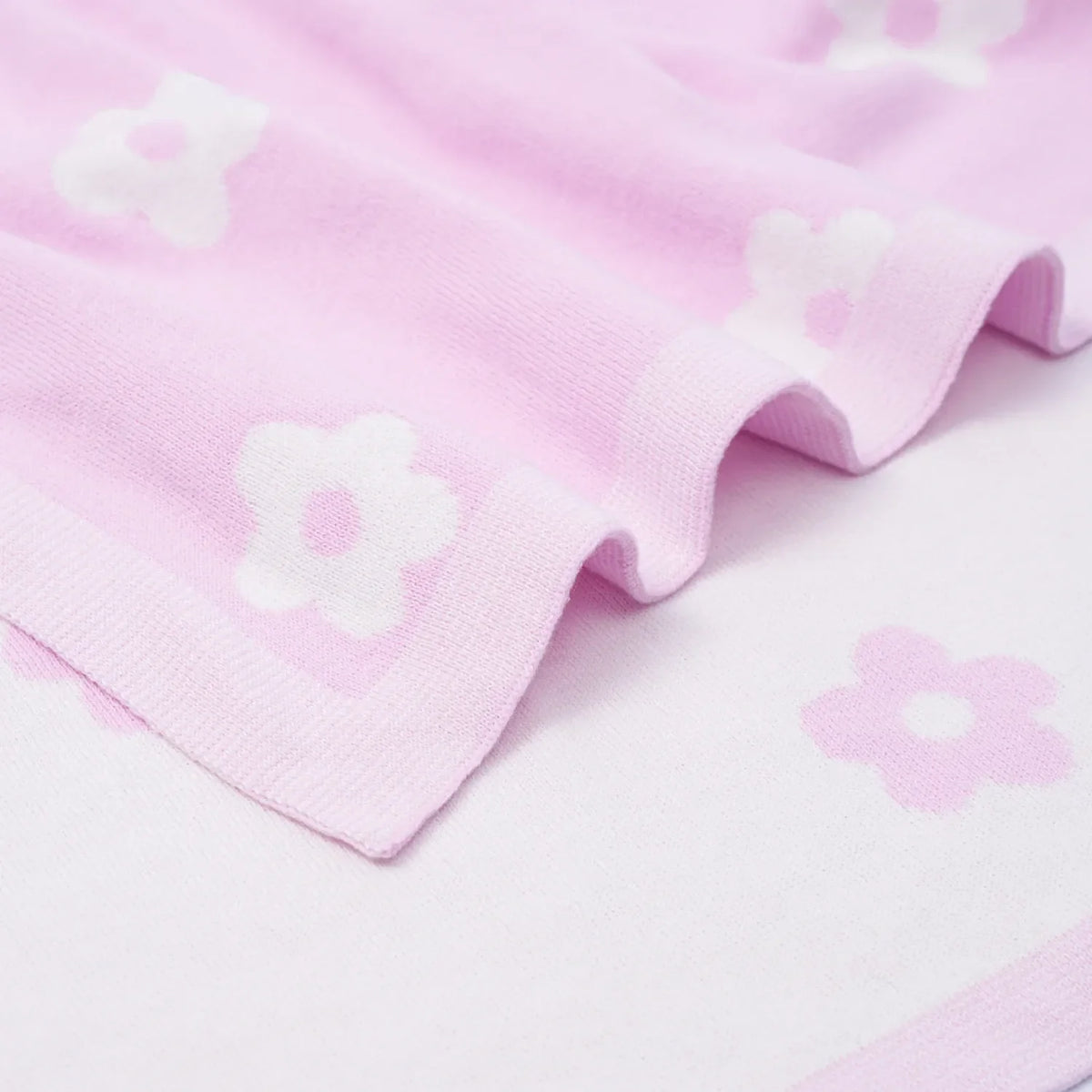 Close-up of ribbed border on pink cotton knit blanket, highlighting woven white daisy motif against soft fabric texture.